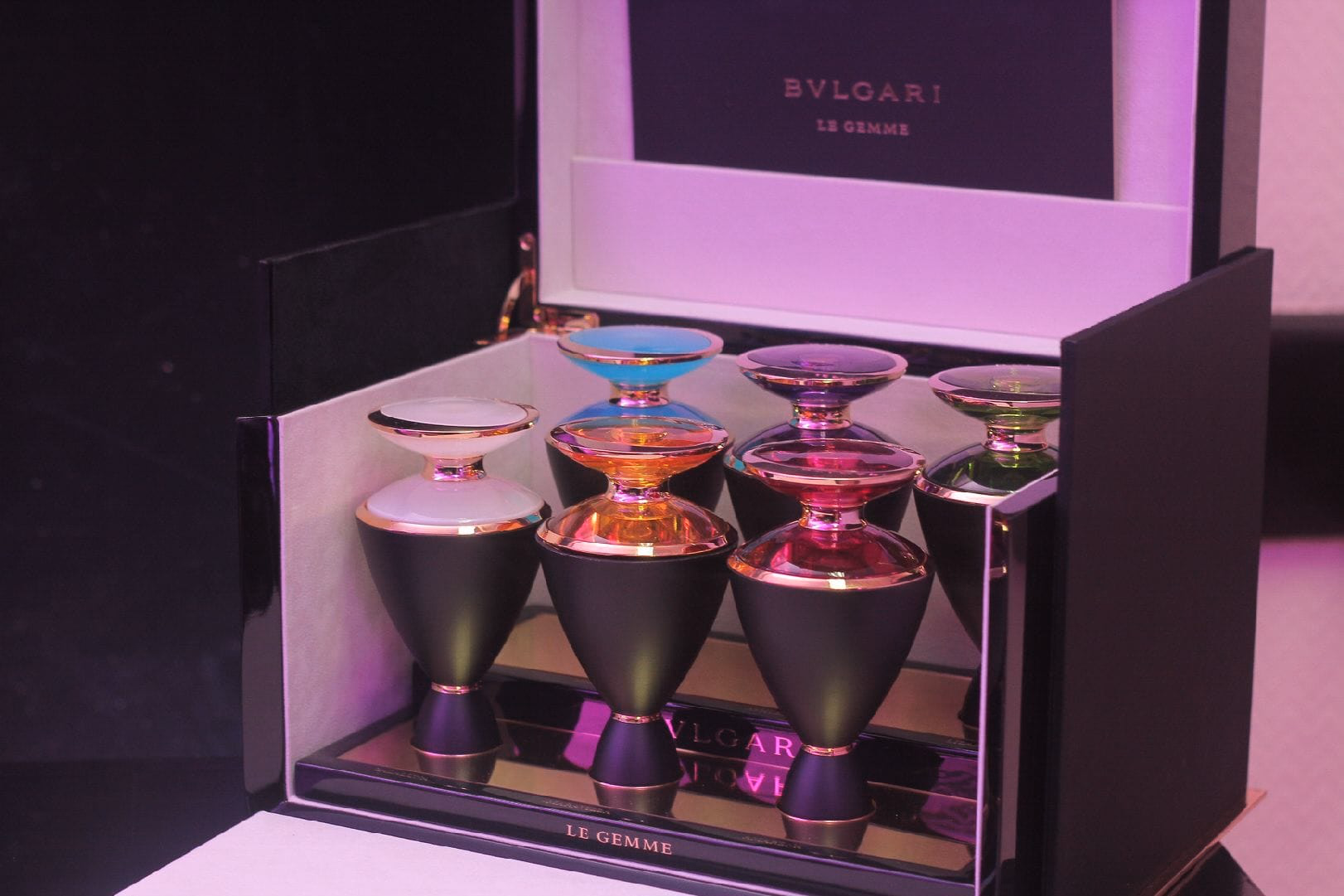 A Bvlgari Le Gemme display case holding iridescent glass bottles in purple and gold, lit from within
