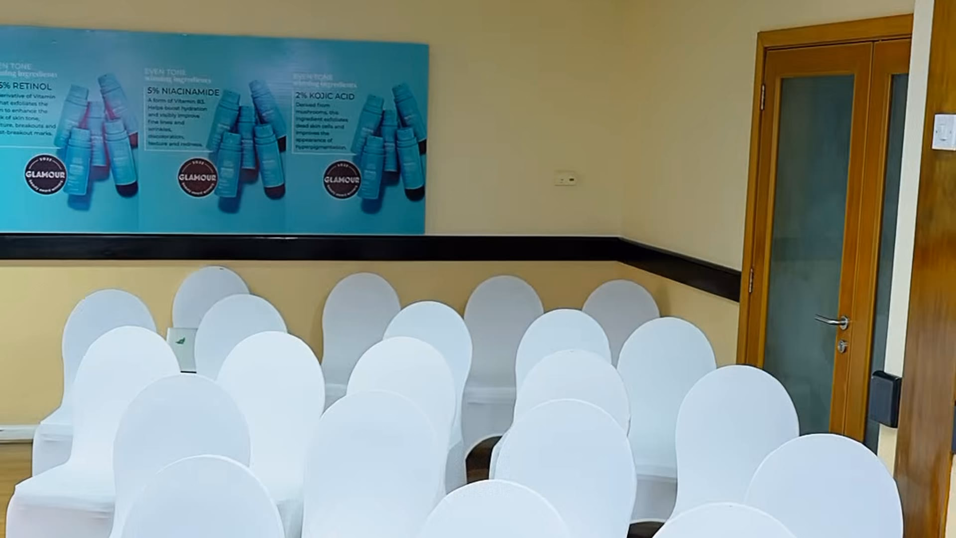 An event room laid out for a skincare launch, with rows of white-covered chairs facing a wall of teal product stands carrying the brand's ingredient panel
