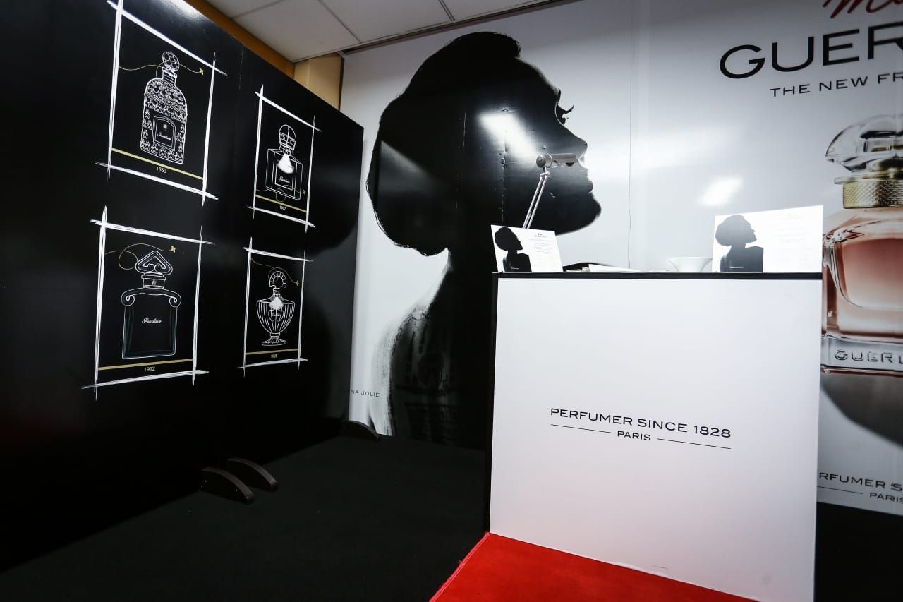 A Guerlain counter installation with a black and white portrait backdrop reading Parfumeur depuis 1828